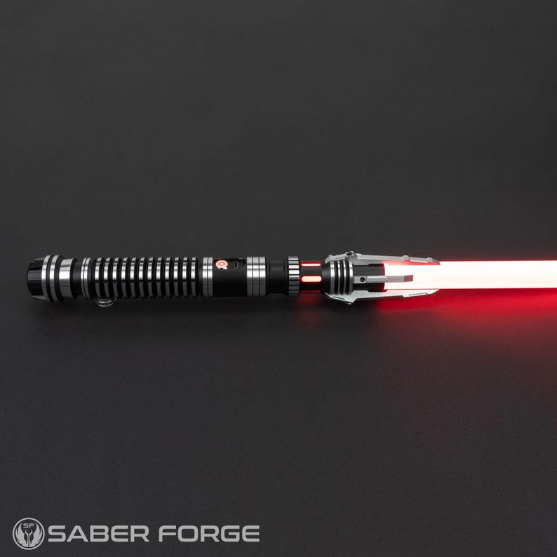 Puede incluir: Un sable de luz negro y plateado con una hoja roja. El sable de luz tiene un agarre texturizado y un emisor plateado.