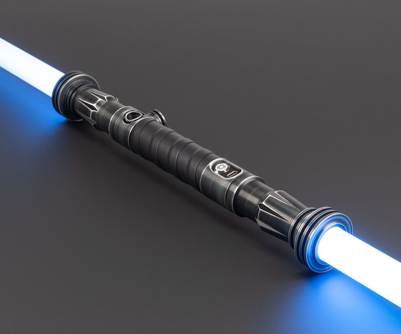 Pode incluir: Um sabre de luz preto com uma l&acirc;mina azul. O sabre de luz tem uma pega texturizada e um acento prateado perto da l&acirc;mina.
