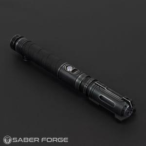 Pode incluir: Um sabre de luz preto com detalhes prateados. O punho tem uma pega texturizada e uma s&eacute;rie de bot&otilde;es e detalhes. A extremidade do sabre de luz tem um design detalhado. O logotipo Saber Forge &eacute; vis&iacute;vel.