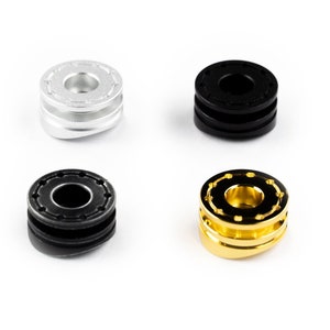 Könnte beinhalten: Vier Metallringe in Silber, Schwarz und Gold. Jeder Ring hat einen erhöhten Außenrand und einen kleineren Innenring. Die Ringe liegen auf einer weißen Oberfläche.