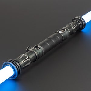 Pode incluir: Um sabre de luz preto com uma l&acirc;mina azul. O sabre de luz tem um acabamento de metal texturizado e um bot&atilde;o prateado no lado.