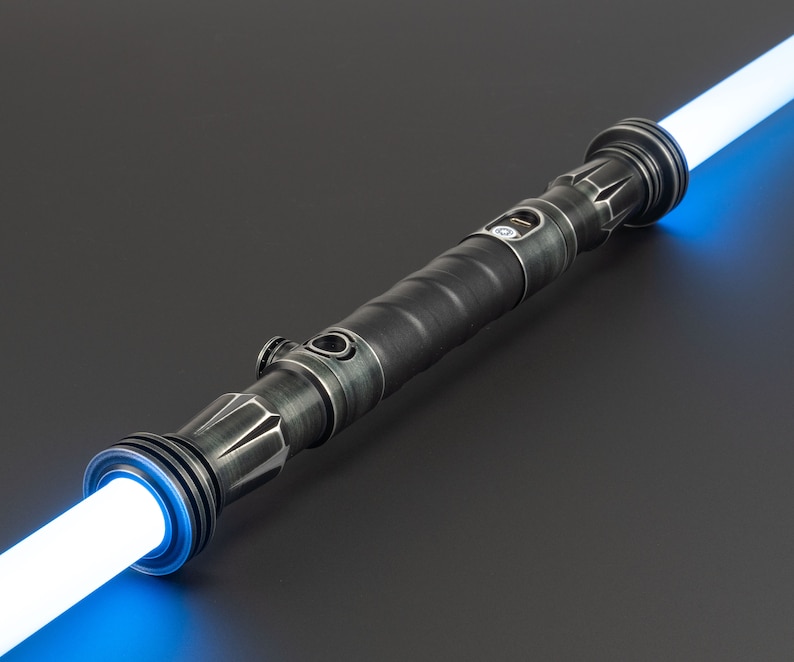 Pode incluir: Um sabre de luz preto com uma l&acirc;mina azul. O sabre de luz tem um acabamento de metal texturizado e um bot&atilde;o prateado no lado.
