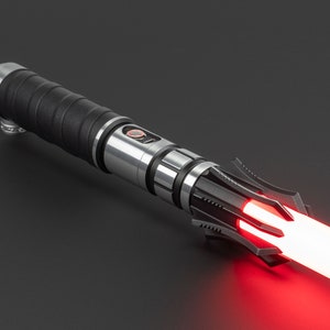 May include: A black and silver lightsaber with a red blade. The lightsaber has a textured black handle and a silver blade holder. The blade is lit and glowing red.