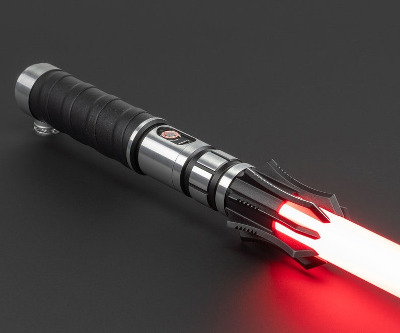 May include: A black and silver lightsaber with a red blade. The lightsaber has a textured black handle and a silver blade holder. The blade is lit and glowing red.