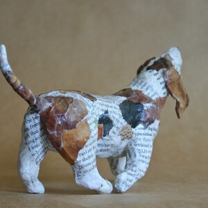 May include: A paper mache sculpture of a brown and white dog with its head tilted back and mouth open. The dog is made from pieces of paper with text printed on them.