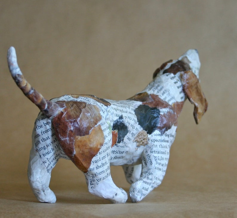 May include: A paper mache sculpture of a brown and white dog with its head tilted back and mouth open. The dog is made from pieces of paper with text printed on them.