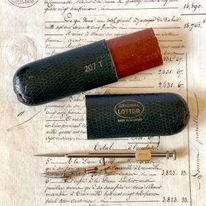May include: An antique drafting set with a dark green leather case and a wooden top. The case is open, revealing a compass and other drawing tools. The text "207 T" is visible on the case.