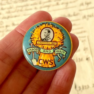 Puede incluir: Un pin redondo vintage con fondo turquesa y borde amarillo. El pin presenta un retrato, el texto "CROWNED 1937" y las palabras "LABOR AND WAIT" con una pala y una hoz. También son visibles las letras "CWS".