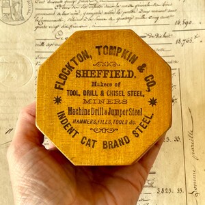 May include: An octagonal wooden box with a yellow finish and black printed text that reads FLOCKTON, TOMPKIN & CO., SHEFFIELD. Makers of TOOL, DRILL & CHISEL STEEL, MINERS, Machine Drill & Jumper Steel, HAMMERS, FILES, TOOLS & CO. INDENT CAT BRAND STEEL.