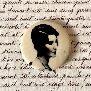 Könnte beinhalten: Ein Vintage-Knopf mit einem Schwarzweiß-Porträt einer Frau mit kurzen Haaren. Der Knopf ist rund und hat einen weißen Hintergrund. Die Frau blickt nach rechts und hat einen ernsten Gesichtsausdruck.