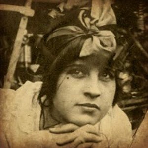 Könnte beinhalten: Sepiafarbenes Porträt einer Frau mit dunklem Haar und einer Schleife. Sie stützt ihr Kinn auf ihre Hände und blickt den Betrachter an. Das Bild hat eine Vintage-Ästhetik.