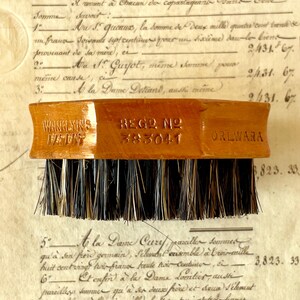 May include: A wooden brush with dark bristles featuring the embossed text WANKLYN'S PATENT, REGD NO 383041, and ORLWARA on the side. The brush has a polished light brown finish and a rectangular shape with slightly curved sides for a firm grip.