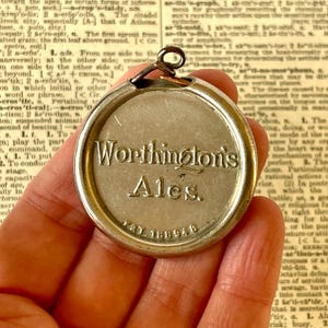 May include: A silver-colored Worthington's Ales medallion with the brand name and "Ales" embossed in a classic font. The medallion has a loop for hanging and the number "188948" is visible.