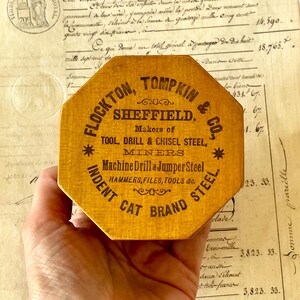 May include: An octagonal yellow wooden box with black printed text reading FLOCKTON, TOMPKIN & CO., SHEFFIELD. Makers of TOOL, DRILL & CHISEL STEEL, MINERS, Machine Drill & Jumper Steel, HAMMERS, FILES, TOOLS etc. INDENT CAT BRAND STEEL.