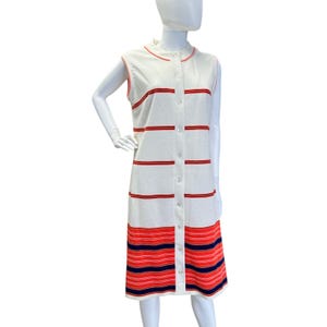 May include: A sleeveless, button-down dress in a mid-length style. The dress is primarily white with horizontal red stripes and a red trim around the collar and armholes. The bottom section features a wider band of red and blue stripes.