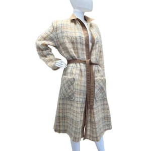 May include: A long, plaid coat in beige, brown, and blue hues, displayed on a mannequin. The coat features a brown belt, collar, and trim, along with two front pockets. The coat is made of a textured fabric.