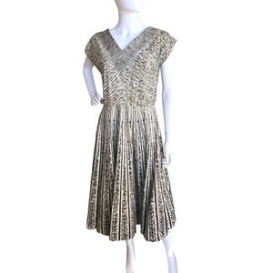 May include: A midi-length dress featuring a V-neckline and short sleeves. The bodice displays a fine, abstract black and white linear pattern, while the skirt showcases a distinct vertical striped design with repeating black leaf motifs.