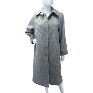 May include: A long, gray wool coat with a button-up front and a classic collar. The coat features a tailored design with a subtle V-shaped seam detail on the front. The coat is displayed on a mannequin.