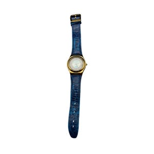May include: A Swatch wristwatch featuring a gold-tone round case and a textured blue leather strap with a crocodile-skin pattern. The watch face has a light-colored dial with gold-tone hands and markers, and the word Swatch is printed on the buckle.