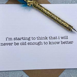 May include: A white card with the text "i'm starting to think that i will never be old enough to know better" printed in black typewriter font.