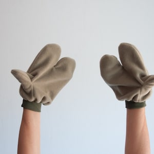 Può includere: Un paio di guanti in pile beige con polsini verdi, tenuti sollevati in aria.