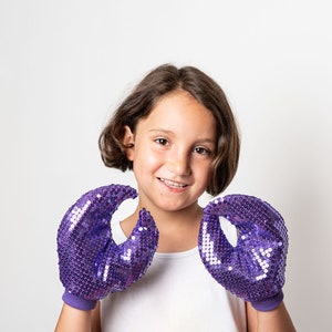 May include: A young person wearing a white shirt and purple sequined gloves with claw-like tips.