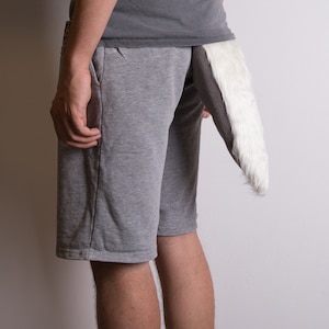 May include: A gray shorts with a white and gray faux fur tail attached. The tail is long and fluffy, with a dark gray stripe down the middle. The shorts are made of a soft material.