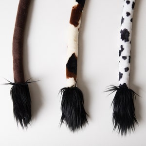 Può includere: Tre code di animali di peluche con punte di pelliccia nera. Le code sono marroni, nere e bianche con macchie marroni, e nere e bianche con macchie bianche.