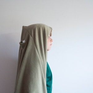 Könnte beinhalten: Ein Kind trägt ein grünes Kapuzenkleid mit einer einzigen Augenöffnung. Das Kind schaut nach rechts.