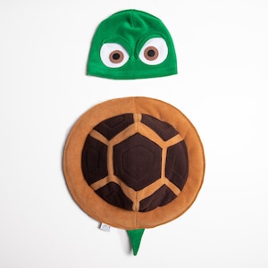May include: A green turtle hat with large eyes and a brown turtle shell costume piece.