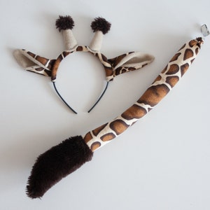 May include: A brown and tan giraffe headband with brown ears and a black headband. A brown and tan giraffe tail with a brown fur tip and a black clip.