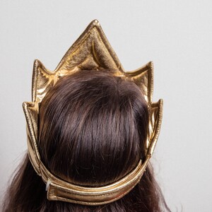 May include: A gold crown headband with a pointed top and a wide band. The headband is made of a soft, flexible material and is designed to fit comfortably on the head.