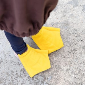 Puede incluir: Un par de fundas para pies de pato con membranas, de color amarillo brillante y hechas de tela suave. Las fundas est&aacute;n dise&ntilde;adas para usarse sobre el calzado, con una forma ancha y plana y detalles de costuras que imitan los dedos palmeados.