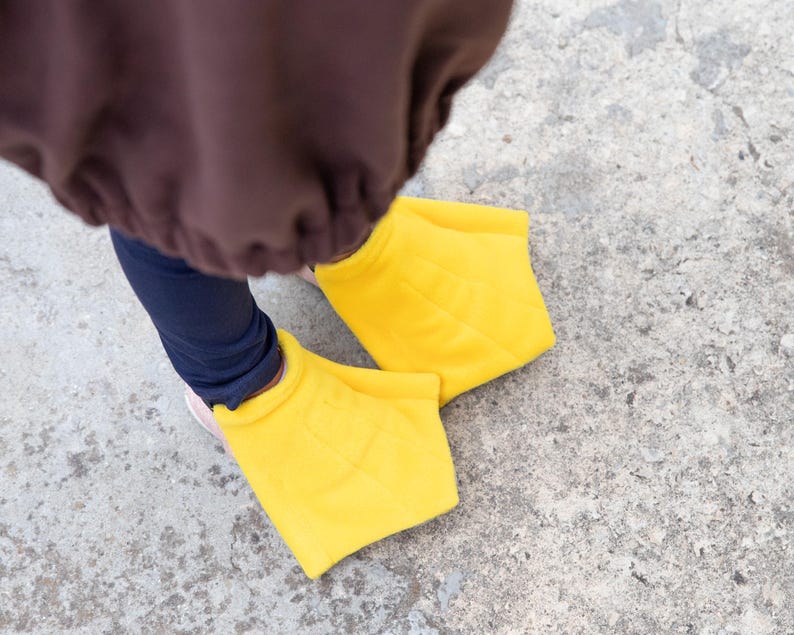Puede incluir: Un par de fundas para pies de pato con membranas, de color amarillo brillante y hechas de tela suave. Las fundas est&aacute;n dise&ntilde;adas para usarse sobre el calzado, con una forma ancha y plana y detalles de costuras que imitan los dedos palmeados.