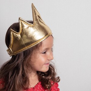 May include: A young girl wearing a gold crown with a red and white polka dot shirt.