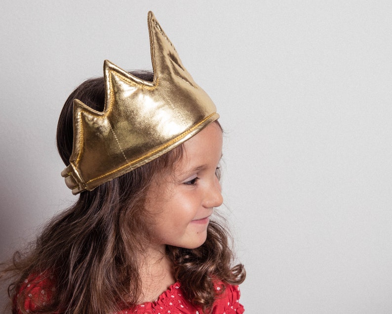 May include: A young girl wearing a gold crown with a red and white polka dot shirt.