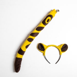May include: A yellow and brown tiger tail costume with a matching headband. The tail is long and fluffy, and the headband has two brown ears.
