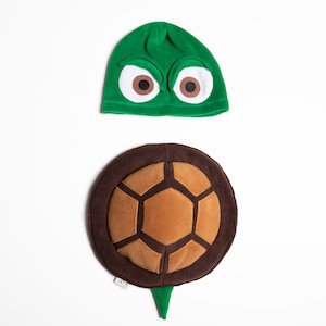May include: A green turtle costume set, comprising a hat with large white-rimmed eyes and brown pupils, and a brown and tan shell-shaped body piece. The costume is designed for children.