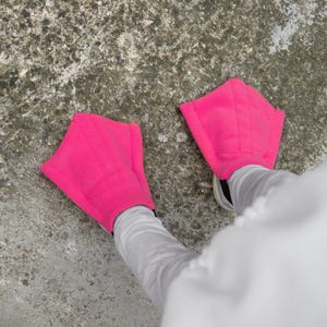 Könnte beinhalten: Ein Paar rosa Stoff-Flossen, die an den Füßen einer Person getragen werden. Die Flossen sind aus weichem, plüschigen Stoff und haben eine einfache, abgerundete Form.