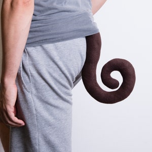 May include: A person wearing grey sweatpants and a grey shirt with a brown curly tail attached to the back of their trousers.