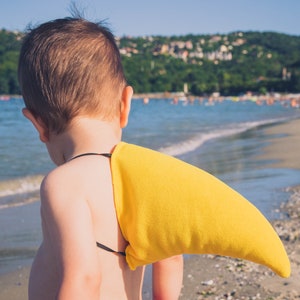 Puede incluir: Un ni&ntilde;o peque&ntilde;o con un disfraz de aleta de tibur&oacute;n amarilla en una playa. El ni&ntilde;o est&aacute; de espaldas a la c&aacute;mara y mirando hacia el oc&eacute;ano.