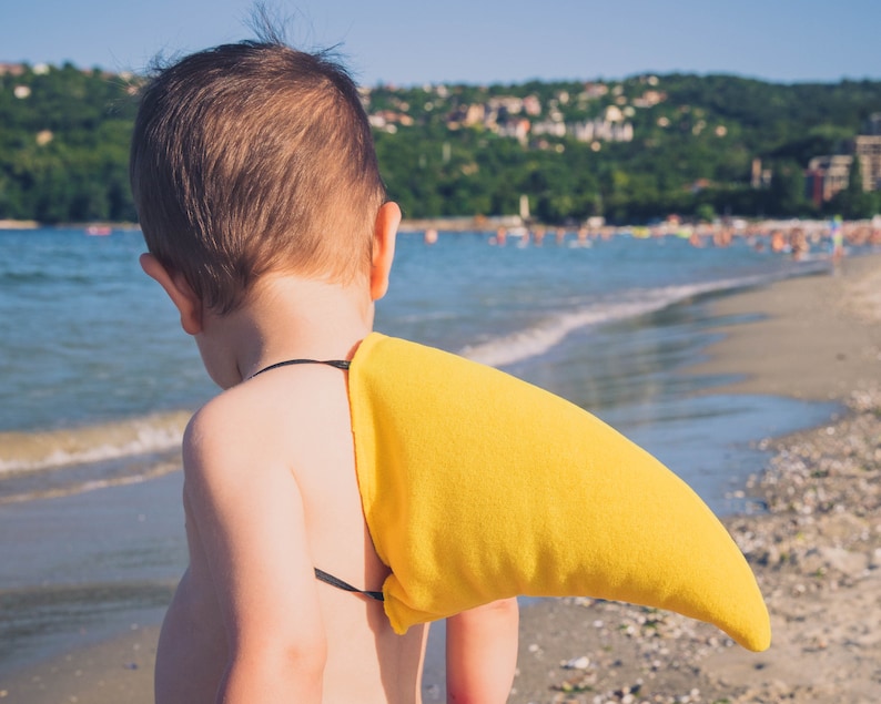 Puede incluir: Un ni&ntilde;o peque&ntilde;o con un disfraz de aleta de tibur&oacute;n amarilla en una playa. El ni&ntilde;o est&aacute; de espaldas a la c&aacute;mara y mirando hacia el oc&eacute;ano.