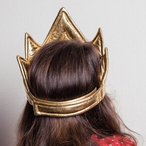 May include: A gold crown with a pointed top and a wide band. The crown is made of a soft, pliable material and is designed to fit comfortably on the head.