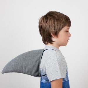 May include: A young boy wearing a grey and blue striped shirt with a grey shark fin attached to the back.