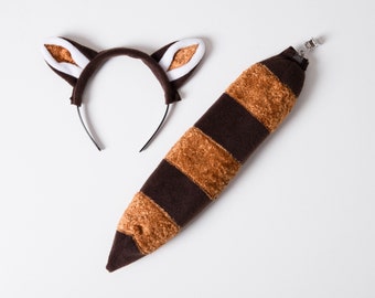 Può includere: Una coda a strisce marroni e beige con un fermaglio e una fascia marrone con orecchie bianche. Questo è un set di costumi da procione per bambini.