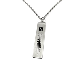 Puede incluir: Un collar de plata con un colgante rectangular que presenta un logotipo de Spotify y un diseño similar a un código de barras.