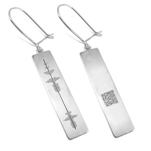 Peut inclure: Une paire de boucles d'oreilles en argent avec un pendentif rectangulaire. Un pendentif présente un motif d'onde sonore, tandis que l'autre présente un code QR.