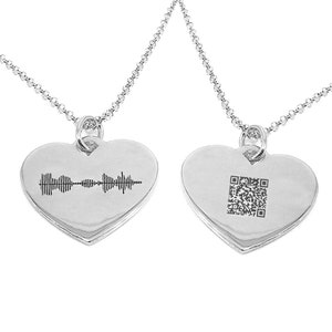 Op de afbeelding: Twee zilveren hartvormige kettingen met kettingen. De ene hanger heeft een geluidsgolf gegraveerd, de andere een QR-code.
