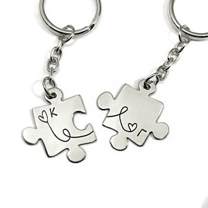 May include: Two silver puzzle piece keychains with a heart and the letters K and L on them.