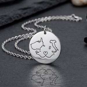 May include: A silver pendant necklace. The round pendant has engraved outlines of two landmasses, possibly representing a connection, with a heart design below. The necklace chain is silver.